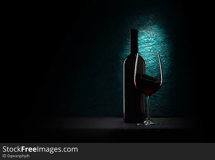 Glass of red wine and bottle on azure stone background, drink against the wall in the old cellar