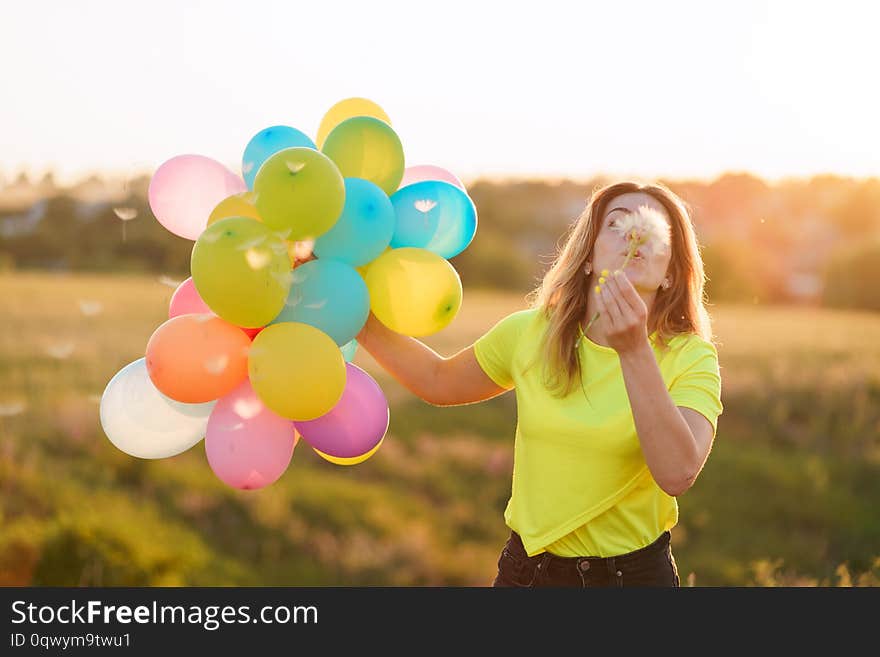 Happy woman with multicolored balloons at sunset