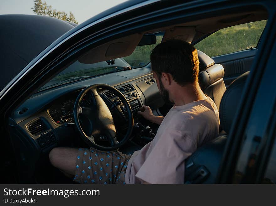 The guy in the pink t-shirt checks the engine of a black car lifting the hood in the country outside the road. The guy in the pink t-shirt checks the engine of a black car lifting the hood in the country outside the road