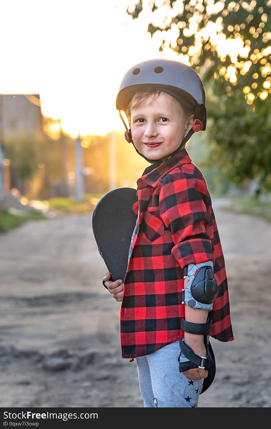 Happy little boy standing on the road holding a skate with his hands. the child defended himself, he put on hand safety gloves