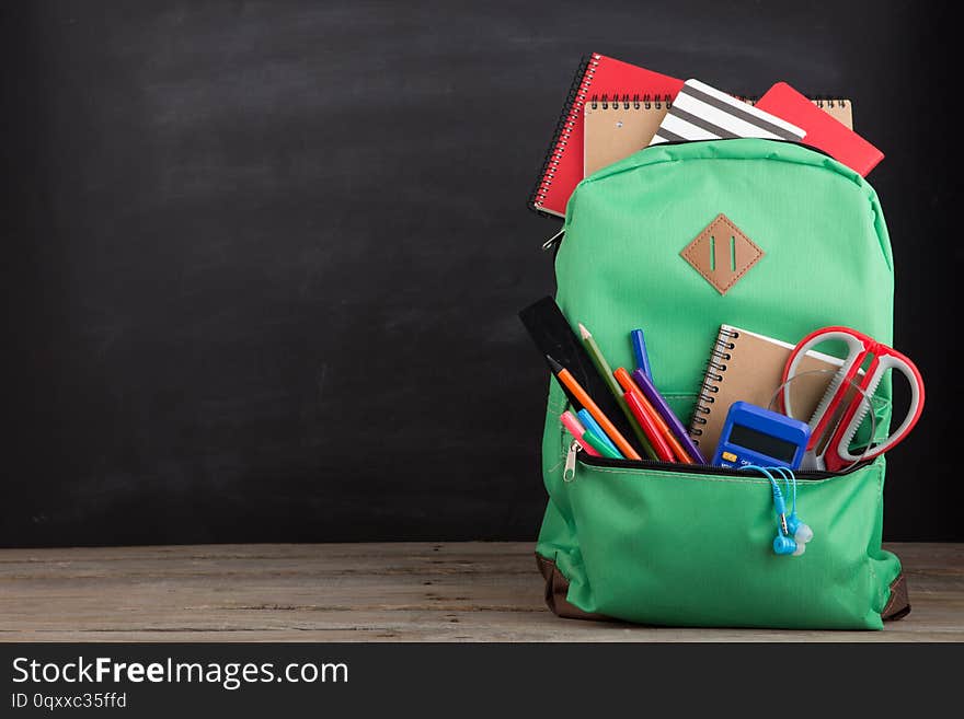 Education concept - school backpack with books and other supplies, blackboard background