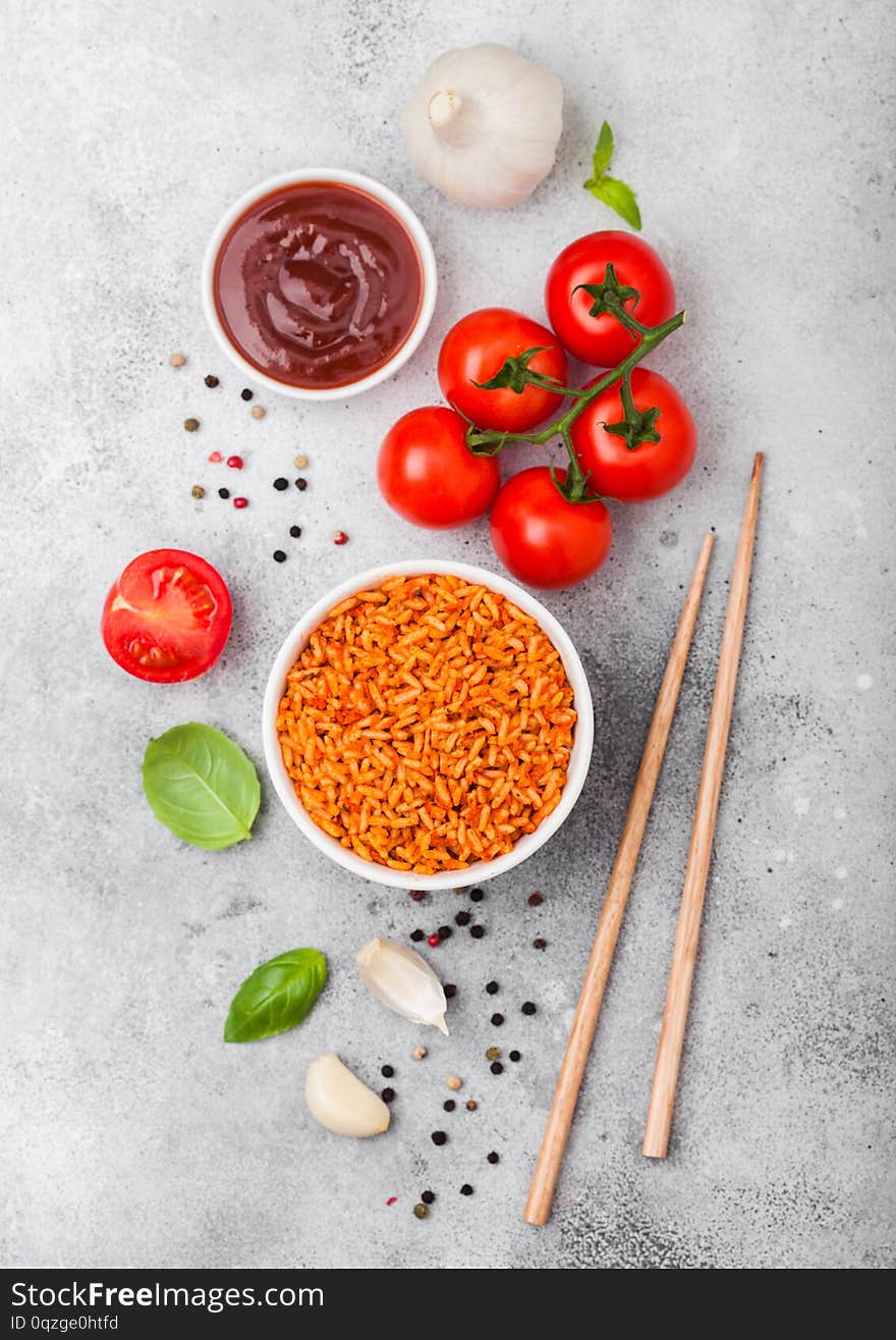 White plate bowl of rice with tomato and basil and garlic and chopsticks on light stone background. Top view