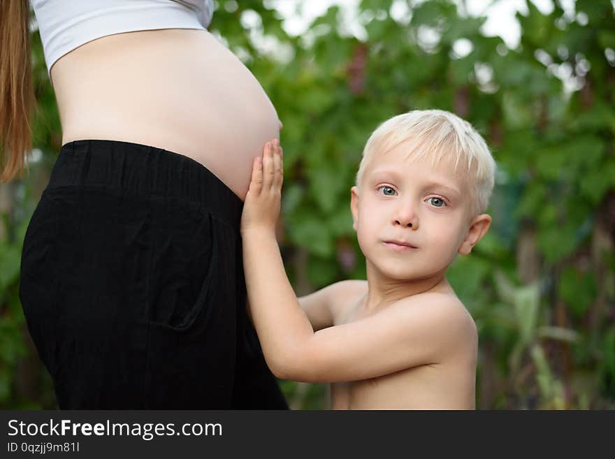 Little blond boy strokes the belly of his pregnant mother. Family concept.