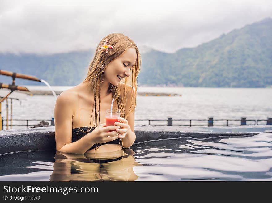 Geothermal spa. Woman relaxing in hot spring pool against the lake. hot springs concept. Drinking guava juice.