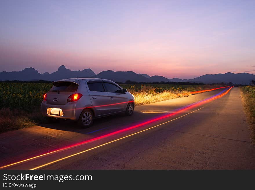 Travel car is parking at the road country side with landscape view beautiful sunset and light trails.