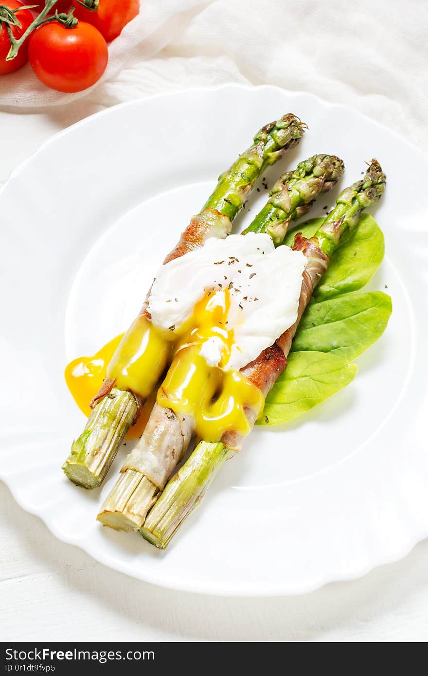 Grilled green asparagus wrapped with bacon, benedict poached egg on white wood background