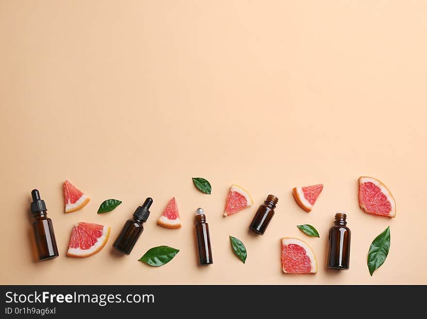 Flat lay composition with grapefruit slices and bottles of essential oil on color background, space for text
