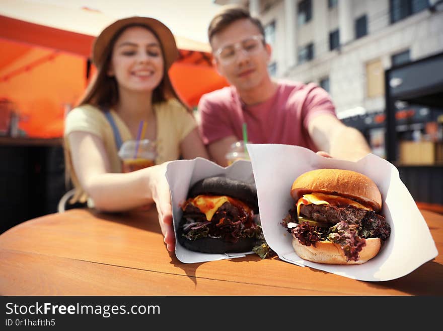 Young Happy Couple With Burgers In Street Cafe