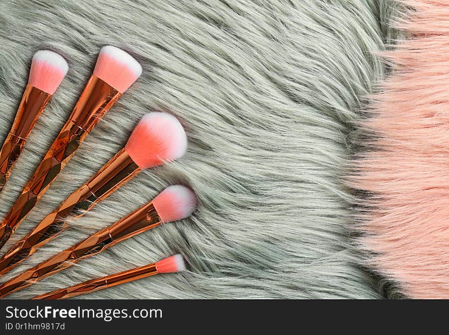 Set of professional makeup brushes on furry fabric, flat lay