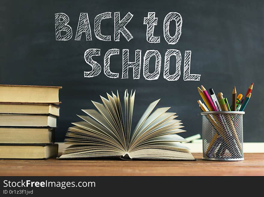 Textbooks and school supplies on a table, against a chalkboard background with chalk. Concept of school with copyspase