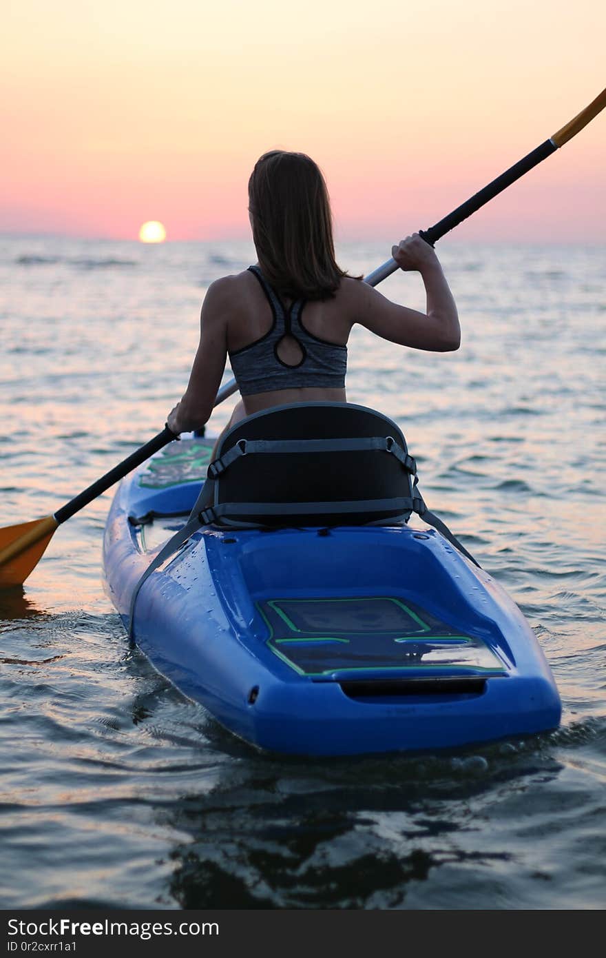 A woman on a kayak rowing in the ocean during a colorful and vibrant sunset, Jericho, Vancouver, British Columbia, Canada. A woman on a kayak rowing in the ocean during a colorful and vibrant sunset, Jericho, Vancouver, British Columbia, Canada