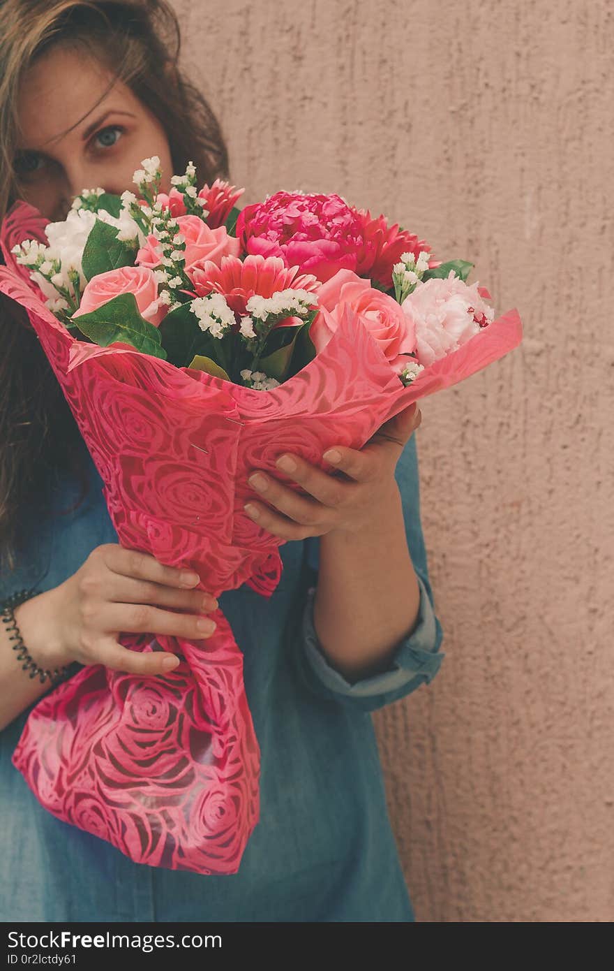 Happy young woman in denim dress with bouquet of gentle fresh flowers