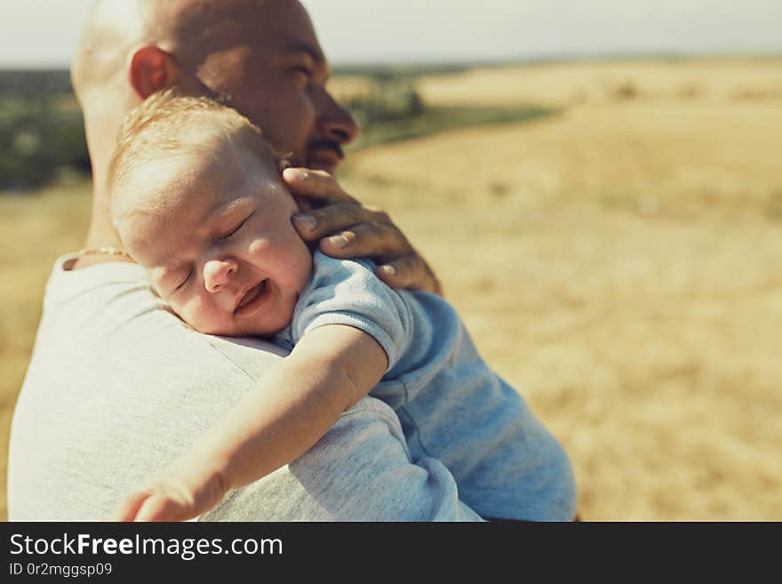 young dad holds a newborn baby on his shoulder, walking in nature. happy father is wearing shorts and a t-shirt. International Father`s Day.