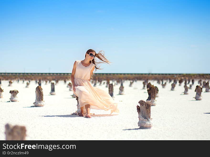 The girl in a white dress with the developing hair sits on a column on the salt lake.