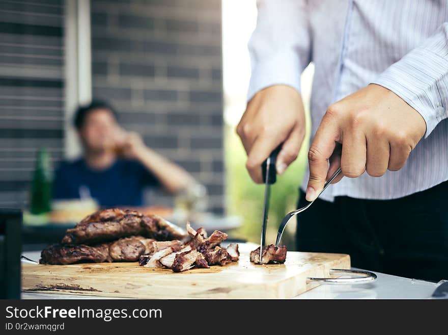 Asian friends are using a knife and a fork to cut the grilled meat on the chopping board to bring food together with friends