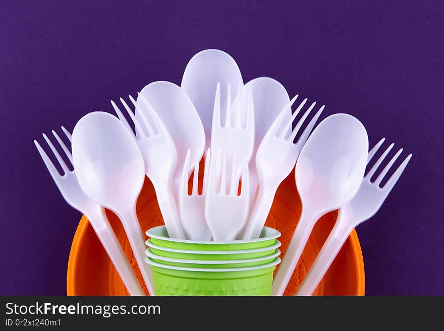 Bright orange and green set of disposable plastic tableware on purple background. Ecology problem. No plastic concept