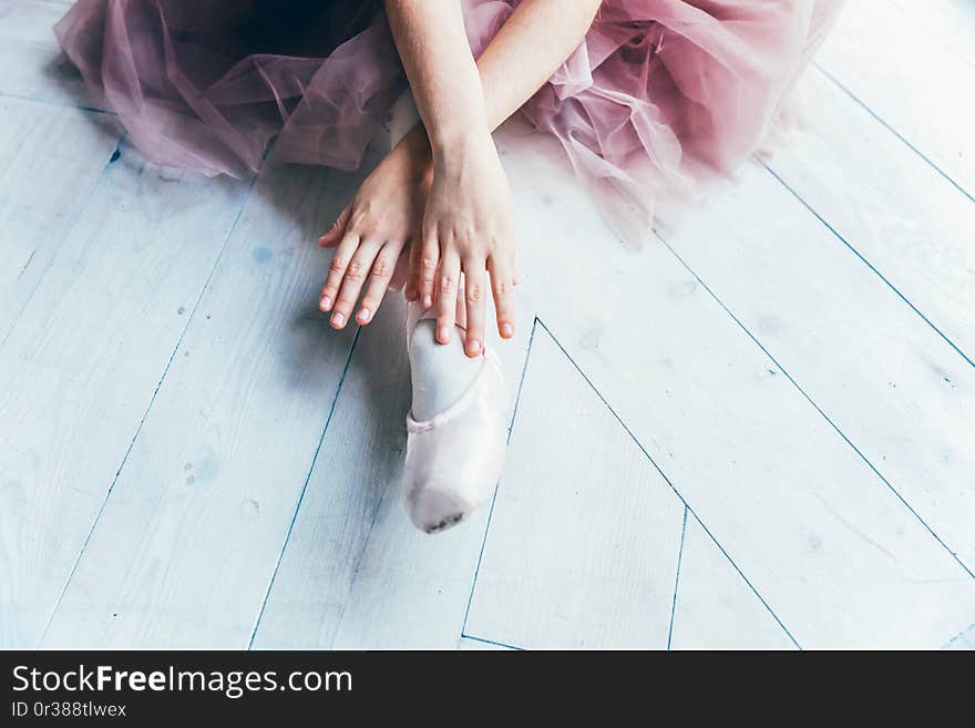 Hands of ballerina in pink tutu skirt puts on pointe shoes on leg in white light hall. Young classical ballet dancer girl in dance class. Hands of ballerina in pink tutu skirt puts on pointe shoes on leg in white light hall. Young classical ballet dancer girl in dance class