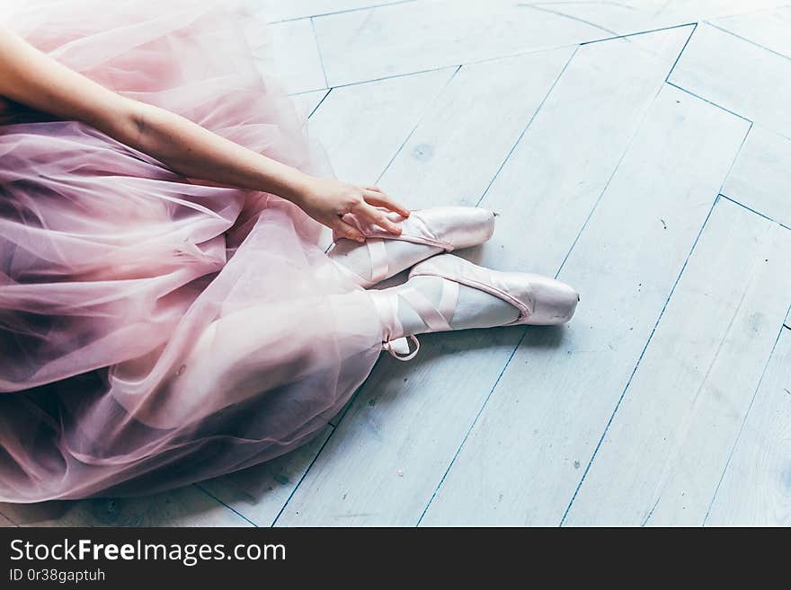 Hands of ballerina in pink tutu skirt puts on pointe shoes on leg in white light hall. Young classical ballet dancer girl in dance class. Hands of ballerina in pink tutu skirt puts on pointe shoes on leg in white light hall. Young classical ballet dancer girl in dance class