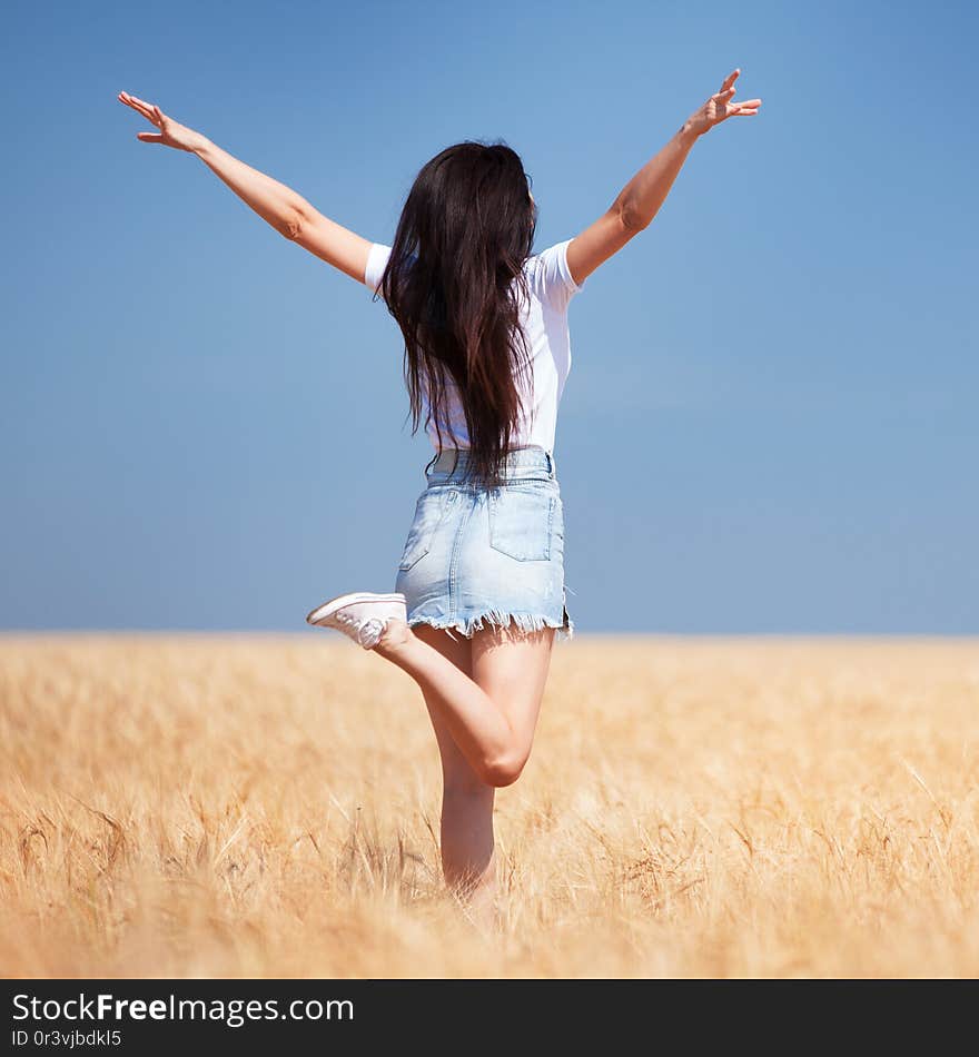 Happy woman enjoying the life in the field Nature beauty, blue sky and field with golden wheat. Outdoor lifestyle. Freedom concept