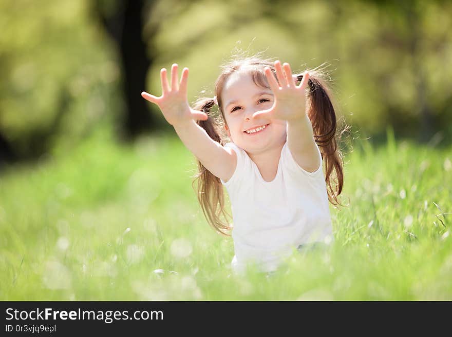 Cute little girl play in the park. Beauty nature scene with colorful background at summer or spring season. Family outdoor lifestyle. Happy girl relax on green grass