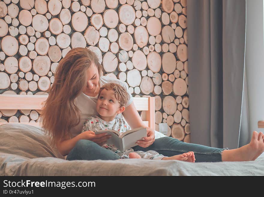 Happy loving family. Pretty young mother reading a book to her little son in modern interior