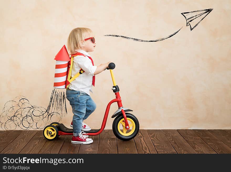 Happy child playing with toy rocket at home. Funny kid driving scooter. Success and win concept