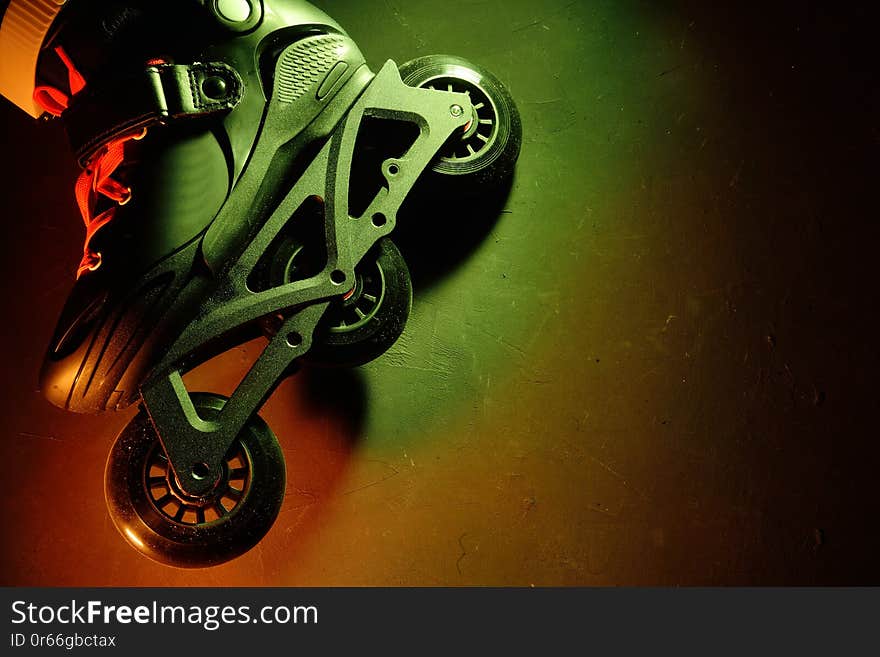 Close up view of roller skates inline skate or rollerblading on dark grunge background in neon yellow green pink light. Sport