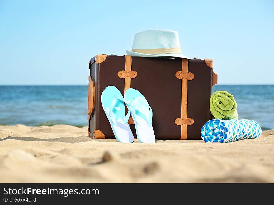 Suitcase and beach accessories on sand near sea. Space for text