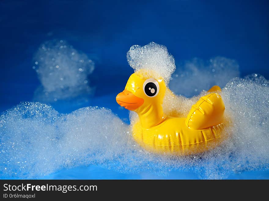 Rubber yellow duck toy on a blue background in foam. Personal hygiene. Bath concept