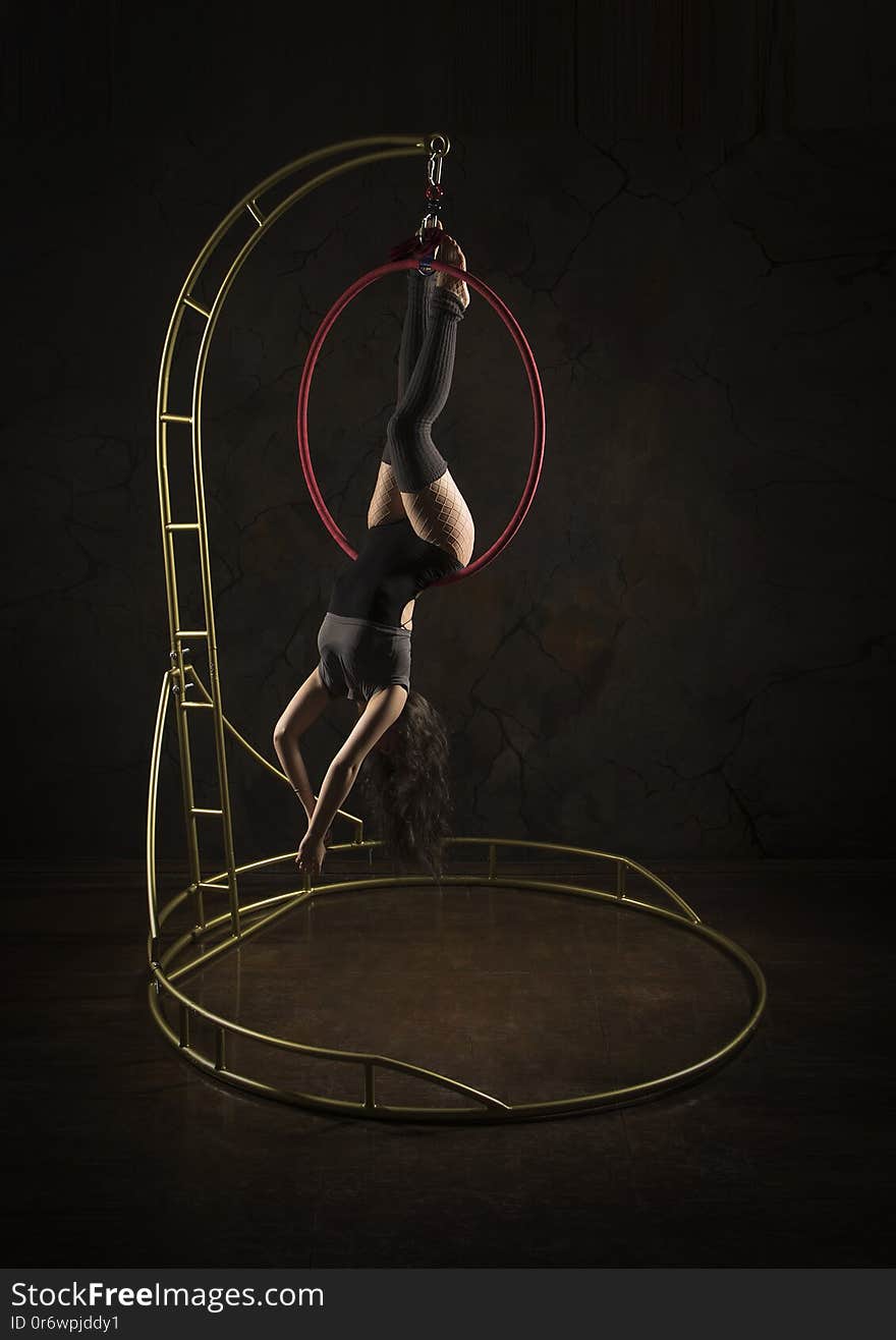 Gorgeous girl, aerial acrobat, in a dark suit performs acrobatic elements on a portable air ring, in the stage light