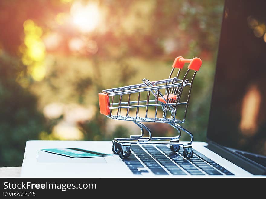 Mini toy trolley, credit card and open laptop on wooden table, copy space, online shopping concept