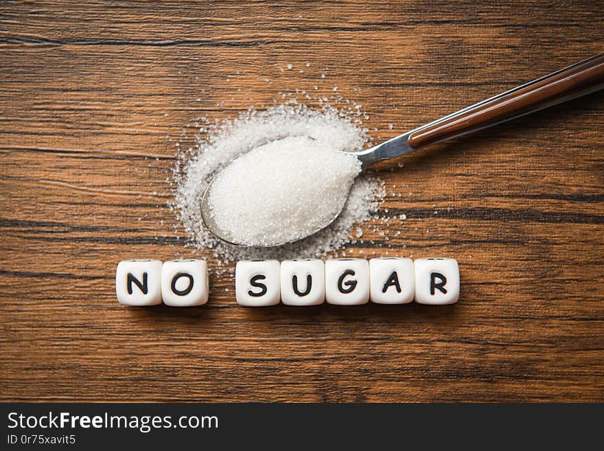 No sugar text blocks with white sugar on spoon wooden background - suggesting dieting and eat less sugar for health concept