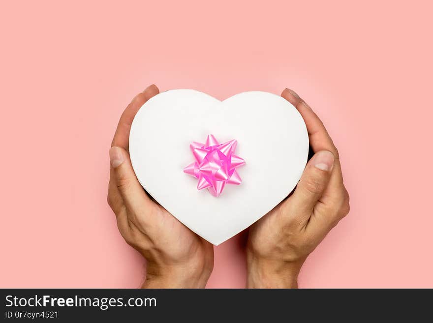 Hands holding craft paper gift box with as a present for Christmas; new year; valentine day or anniversary on pink background