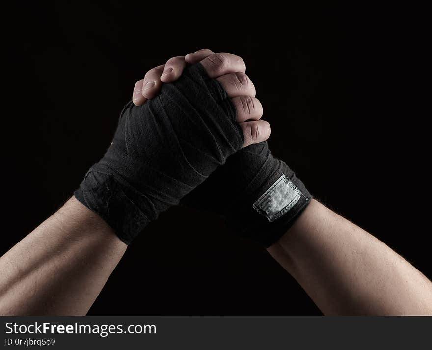 gesture of friendship, two male hands of an athlete tied with a black textile bandage, black background