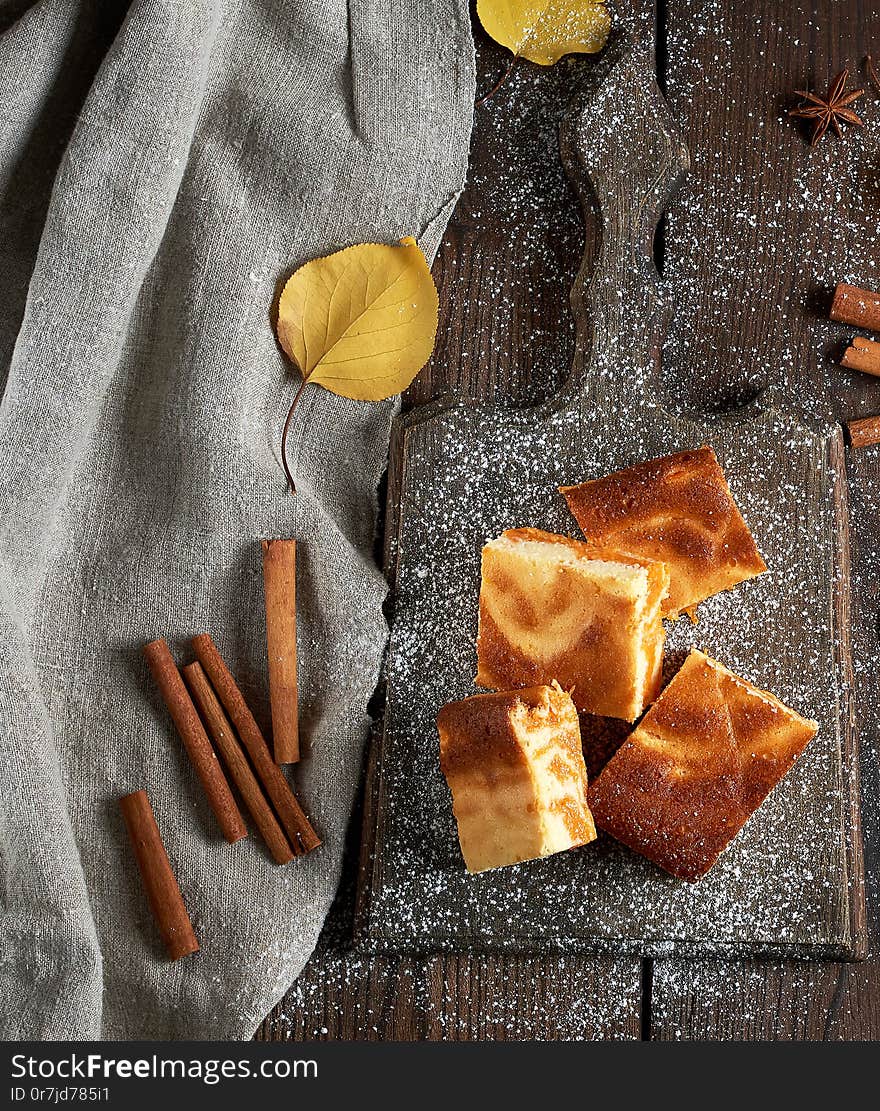 square slices of cottage cheese and pumpkin pie on a wooden board, dessert is sprinkled with icing sugar, top view