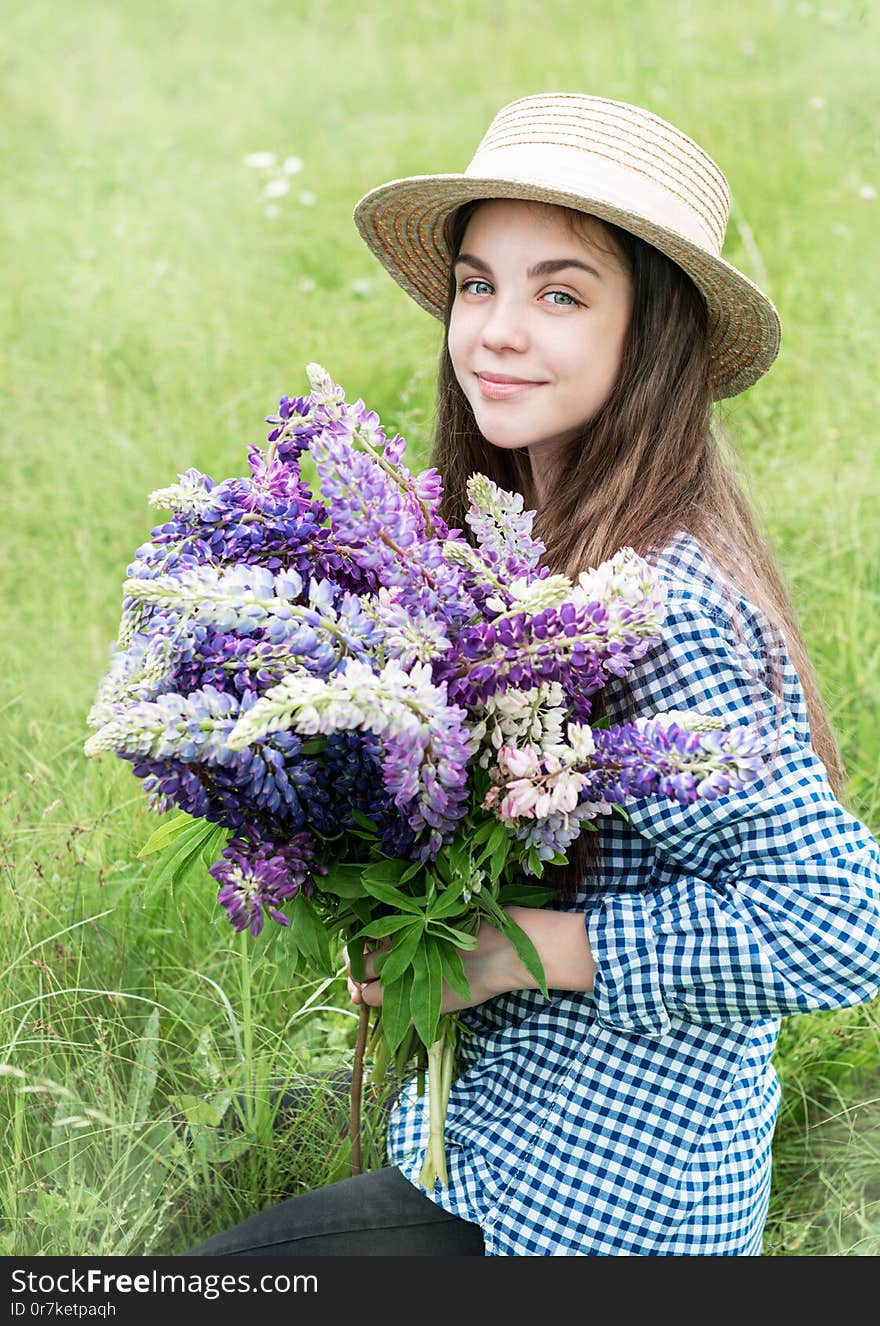 Girl in a summer field with a straw hat and a bouquet of lupins