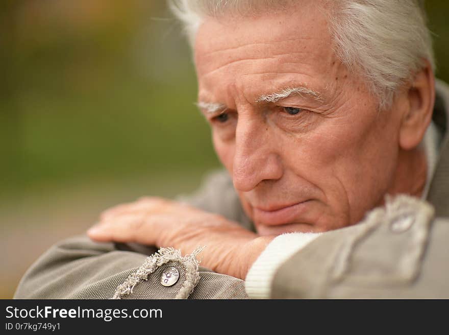 Portrait of sad senior man posing in autumn park