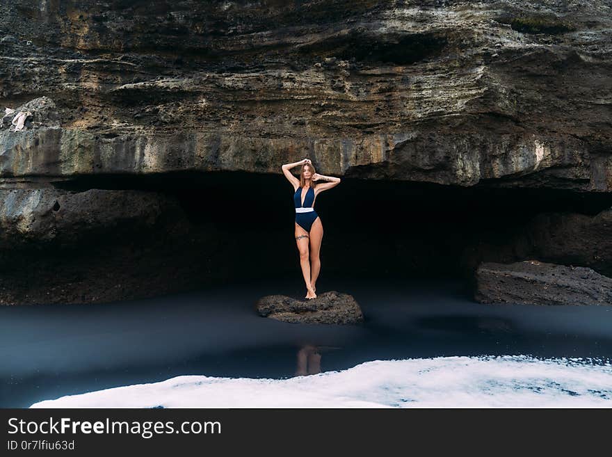 Sexy girl poses in blue swimsuit near cave on black sand beach, concept travel