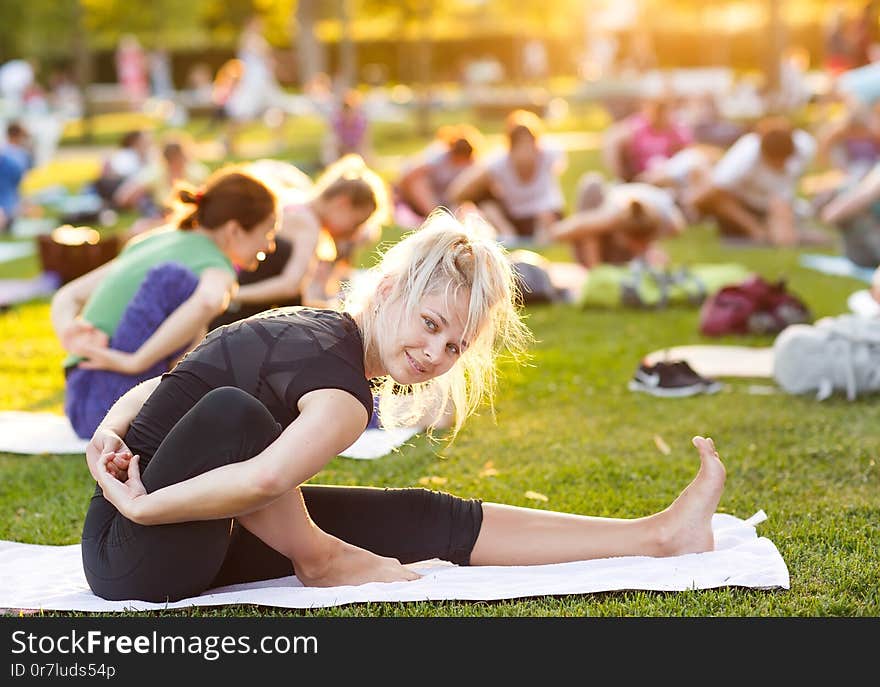 Big group of adults attending a yoga class outside in park