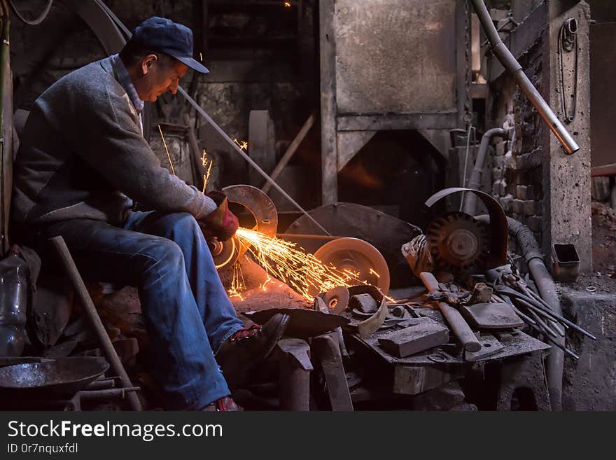 The blacksmith polishing metal products making sparks while using a grinding machine in his traditional workshop