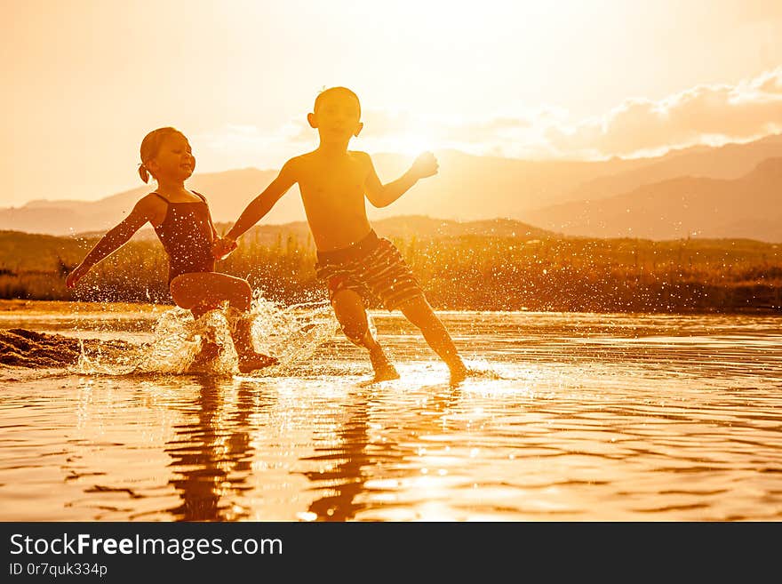 Portrait of two children aged 3 and 6 playing in the sea and spraying water around them. Backlight image at sunset