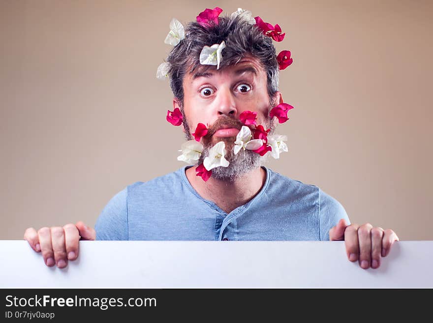 Handsome surprised man with flowers on beard and hair. People, emotions, summer or spring concept