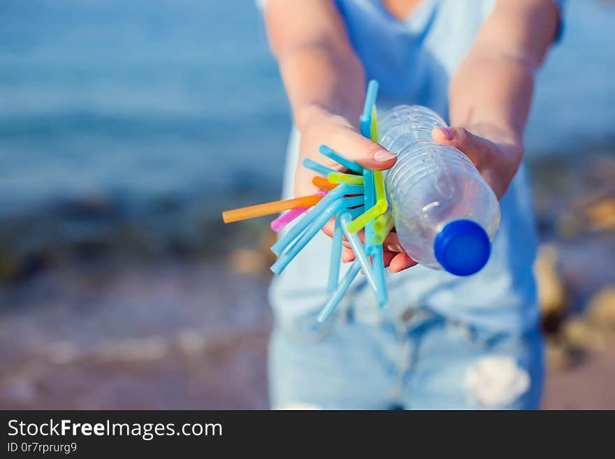 Woman holds plastic bottle and straws in hands on the beach. Beat Plastic Pollution concept