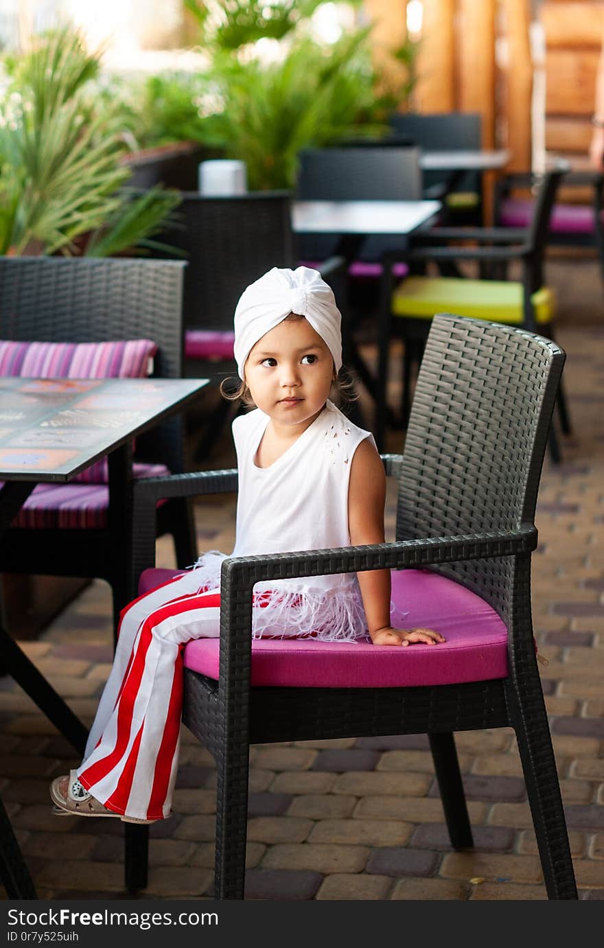 Stylish little girl with white turban on her head sitting in a cafe