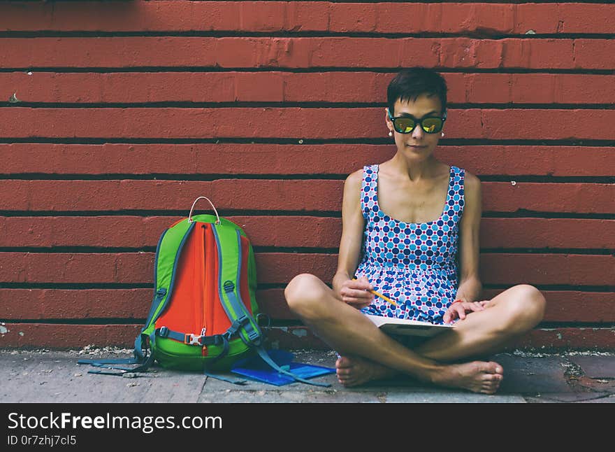 Barefoot girl draws sitting near a brick wall