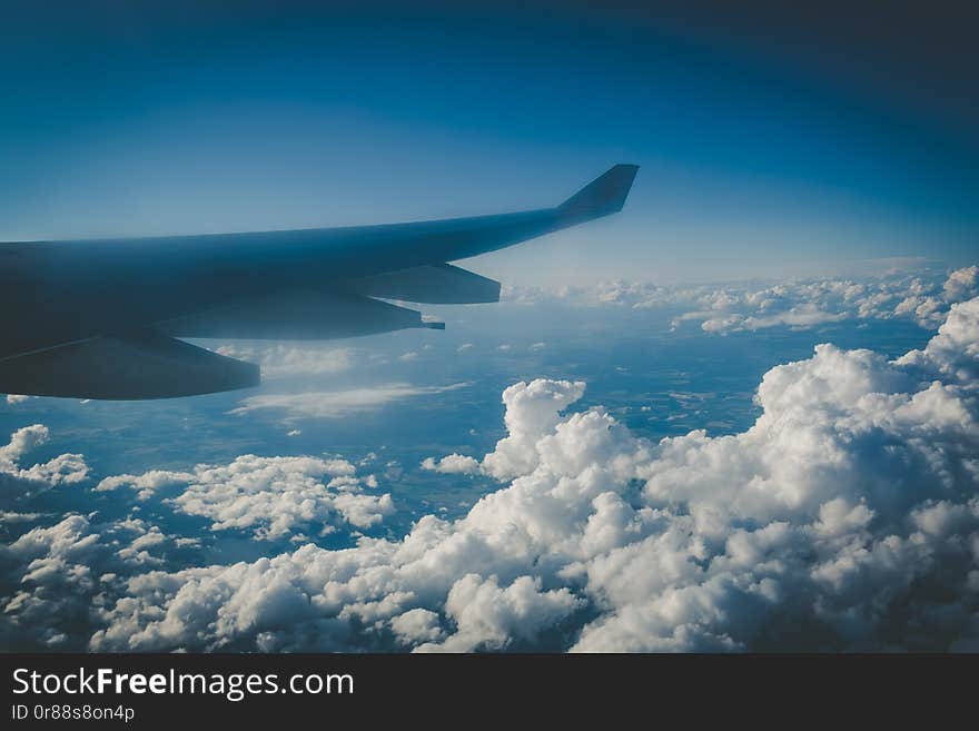 Wing of large passenger jet in mid flight above fluffy clouds and distant earth. Wing of large passenger jet in mid flight above fluffy clouds and distant earth