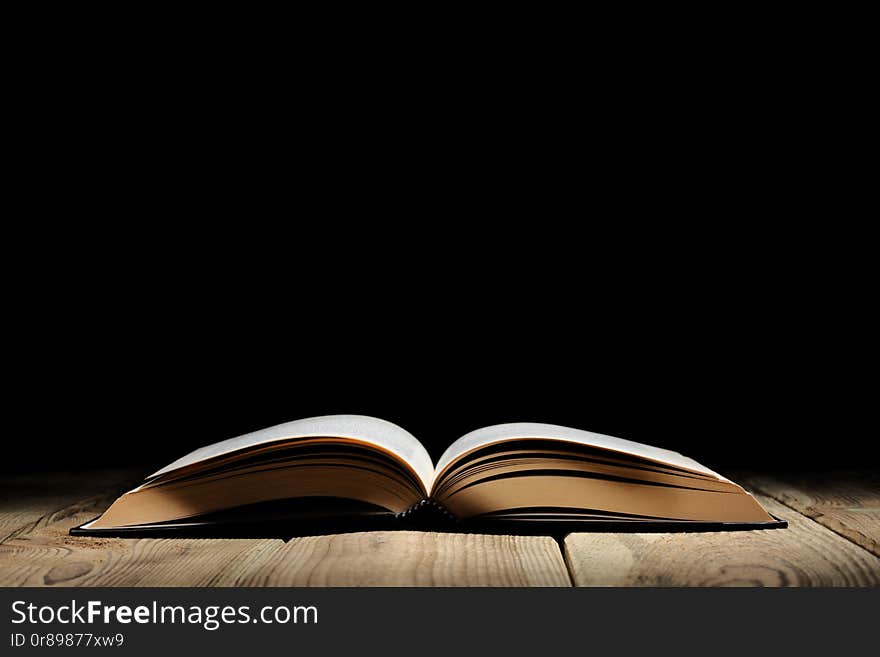 Open book on a wooden table and black background  with copy space for your text