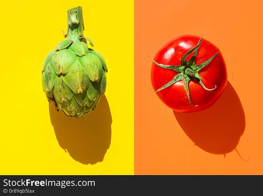 Ripe green artichoke red tomato on duotone yellow orange background with hard light harsh shadows. Trendy funky creative style for food poster banner of Mediterranean cuisine vegan concept