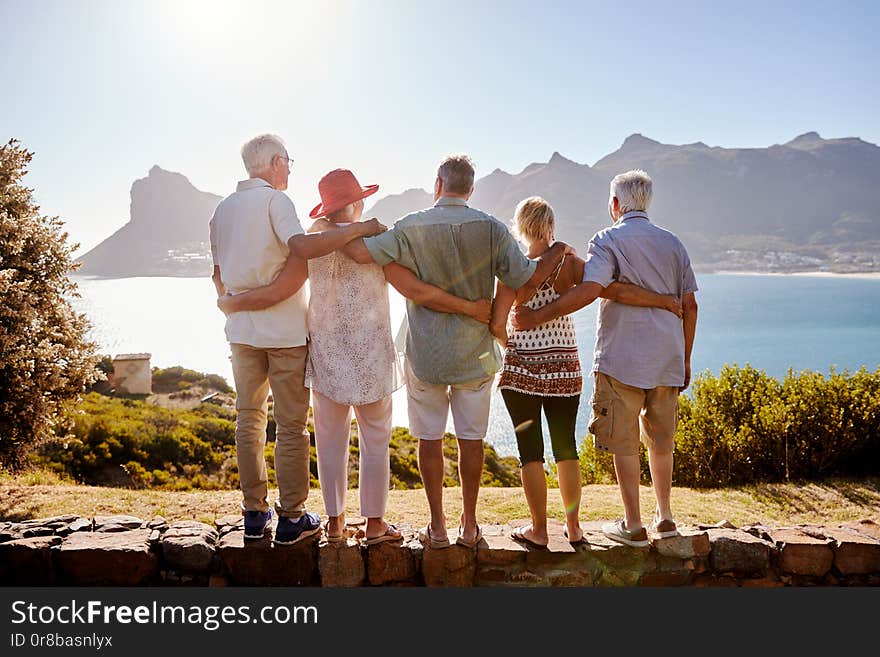 Rear View Of Senior Friends Visiting Tourist Landmark On Group Vacation Standing On Wall