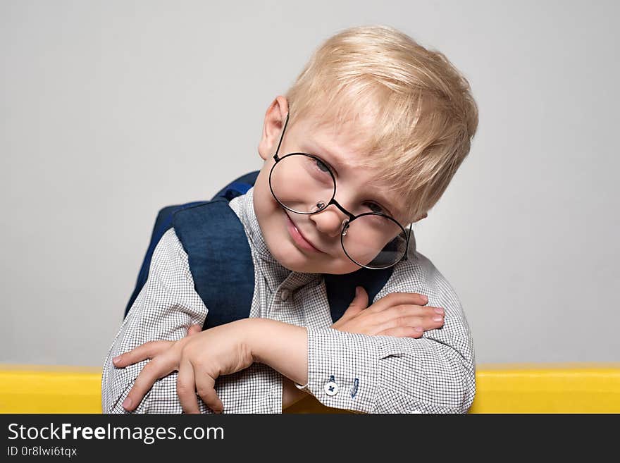 Portrait of a blond smiling boy in glasses and with a school backpack on a white background. School concept.